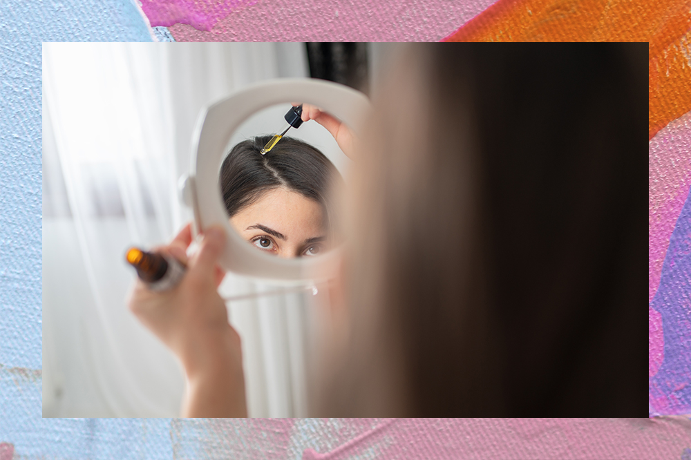 Mulher segurando espelho enquanto aplica sérum na raiz do cabelo. Montagem em fundo rosa, azul e laranja