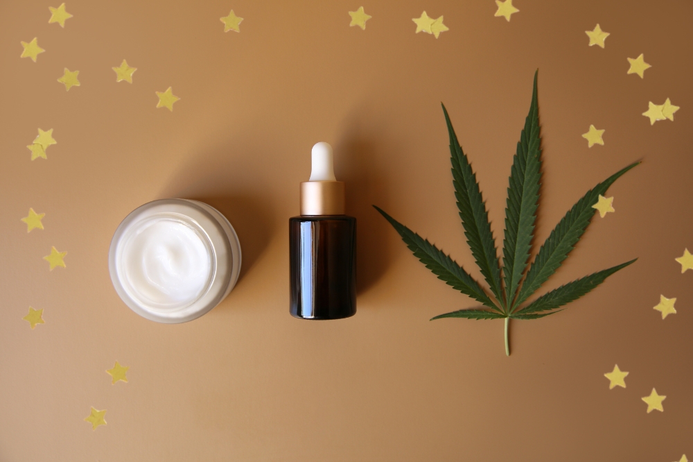 Foto com dois produtos de beleza e uma folha de cannabis com detalhe de estrelas douradas nas bordas.
