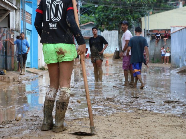 Pessoa com enxada retira lama em bairro do litoral