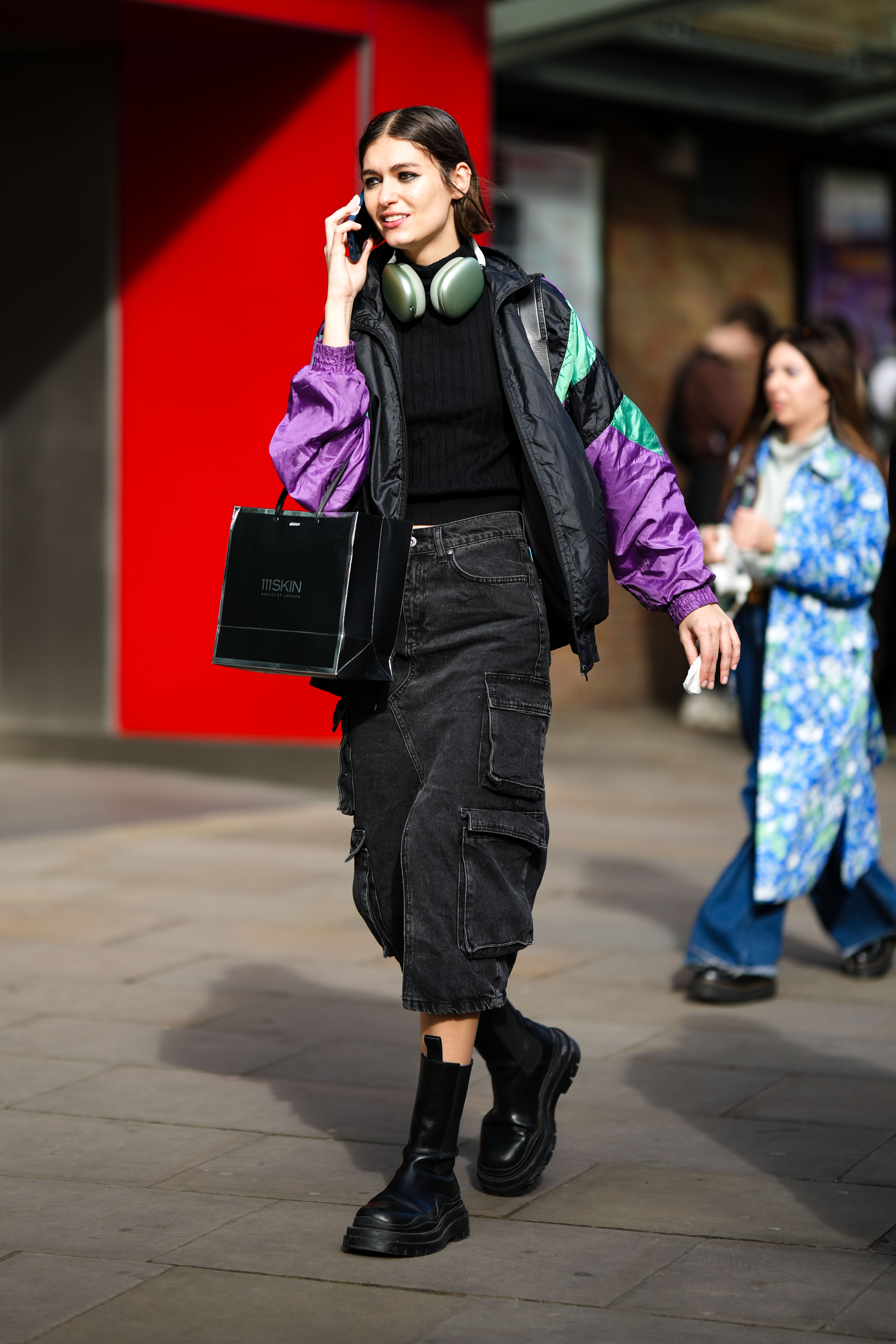 Look com camiseta preta, jaqueta bomber, saia cargo e bota preta no street style da semana de moda de Londres