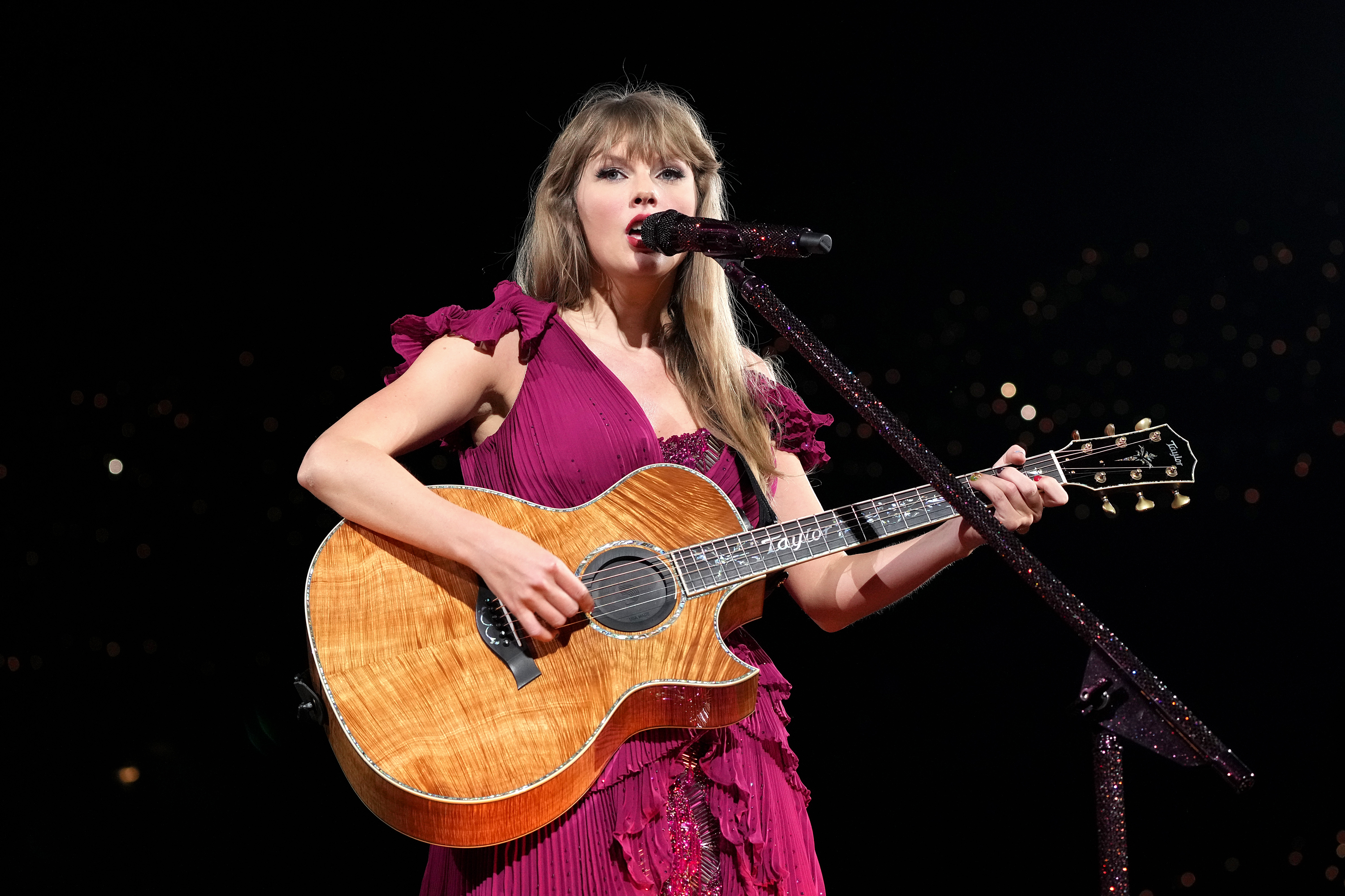 Taylor Swift no primeiro show da The Eras Tour tocando violão e usando vestido na cor vinho