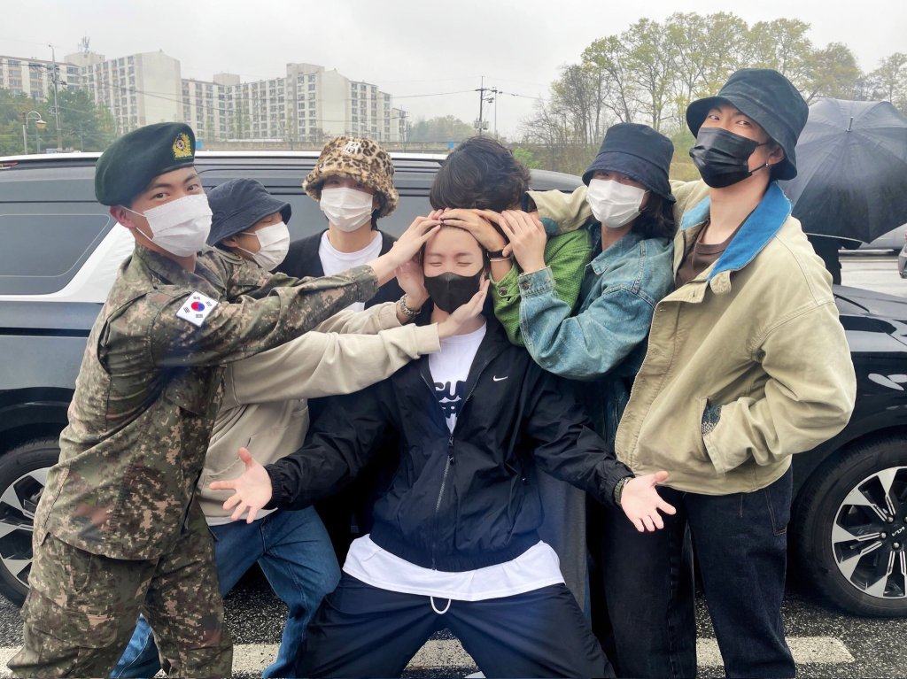 Imagem dos integrantes do BTS reunidos e com as mãos na cabeça de J-Hope