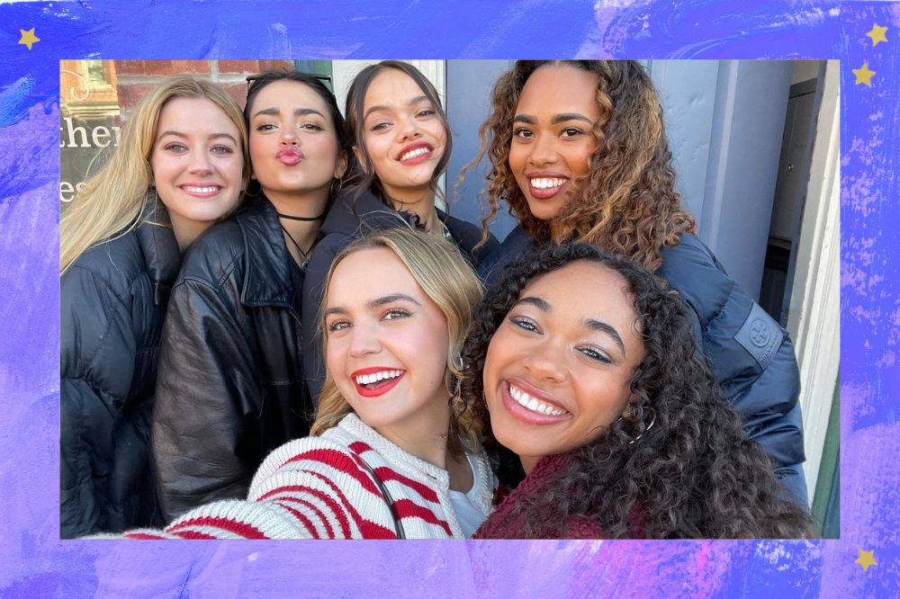 Selfie das atrizes do elenco do reboot de Pretty Little Liars; elas estão reunidas e sorrindo para foto; a margem é uma textura em tons de lilás, azul, roxo e branco com estrelas amarelas como decoração