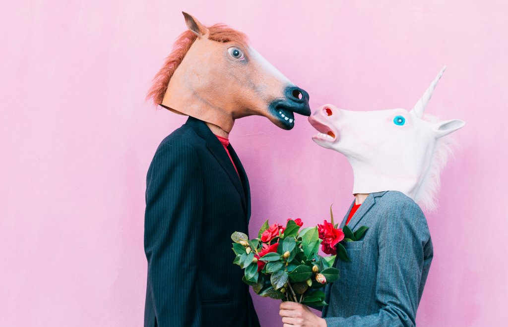 Um casal vestindo máscaras de cavalo se beijando e segurando um buquê de flores