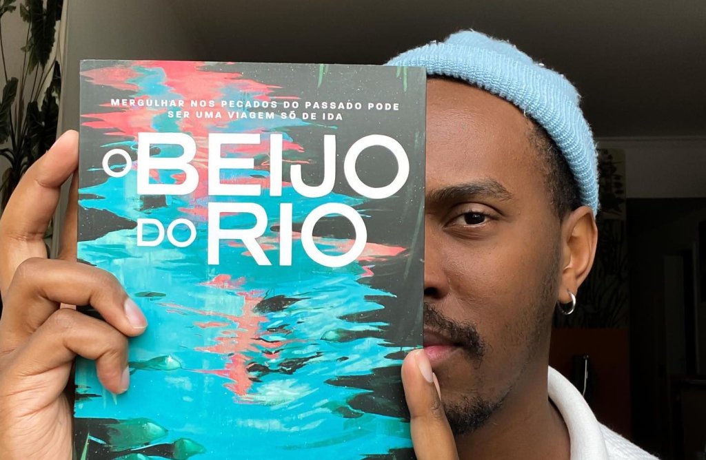 Volp segura o livro O Beijo do Rio na altura do rosto, escondendo um de seus lados