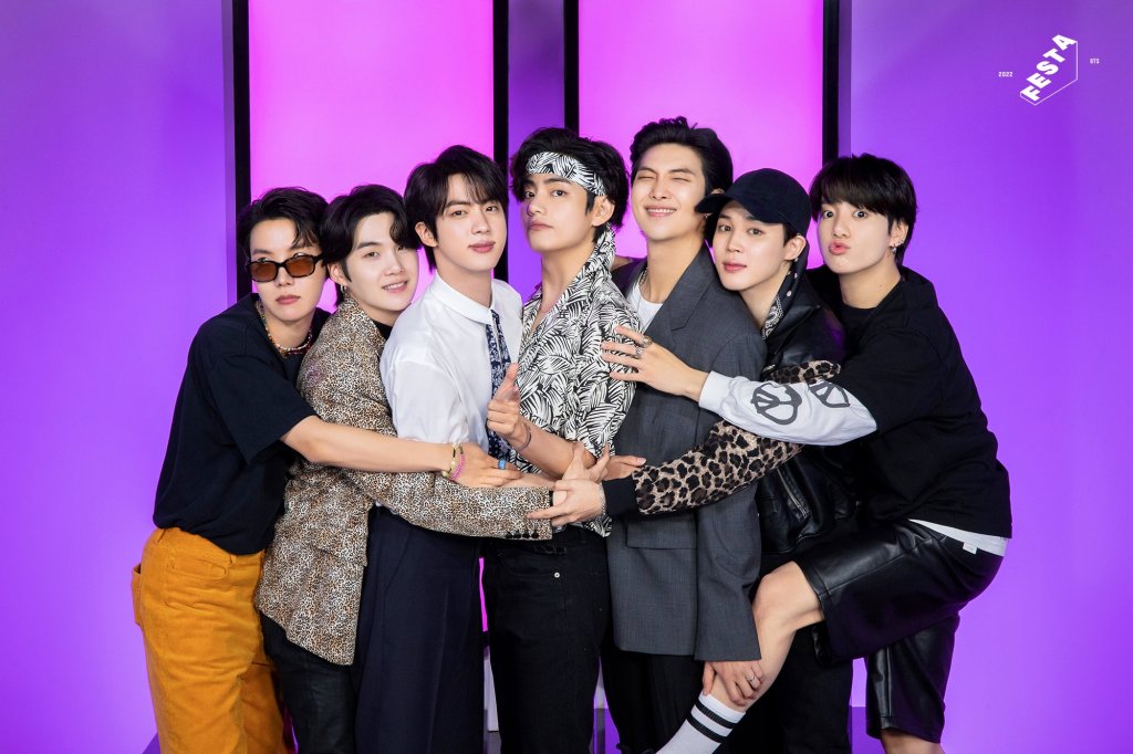 Integrantes do BTS abraçados enquanto posam para fotos com luzes lilás e roxas ao fundo