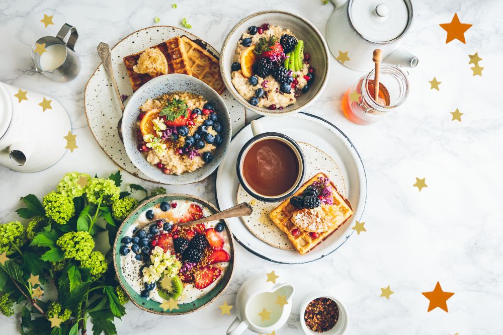 Foto de cima de uma mesa branca, com pratos e bowls, com frutas, mel e leite