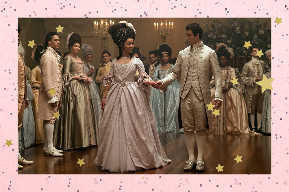 Montagem em fundo rosa com bolinhas e estrelas douradas de foto de cena da série Rainha Charlotte, spin-off de Bridgerton, da Netflix. Na foto, acontece um baile real, e no plano principal estão a Rainha Charlotte e o Rei George.