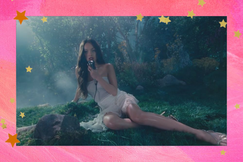 Olivia Rodrigo no clipe da música Vampire. Fundo rosa com estrelas douradas.