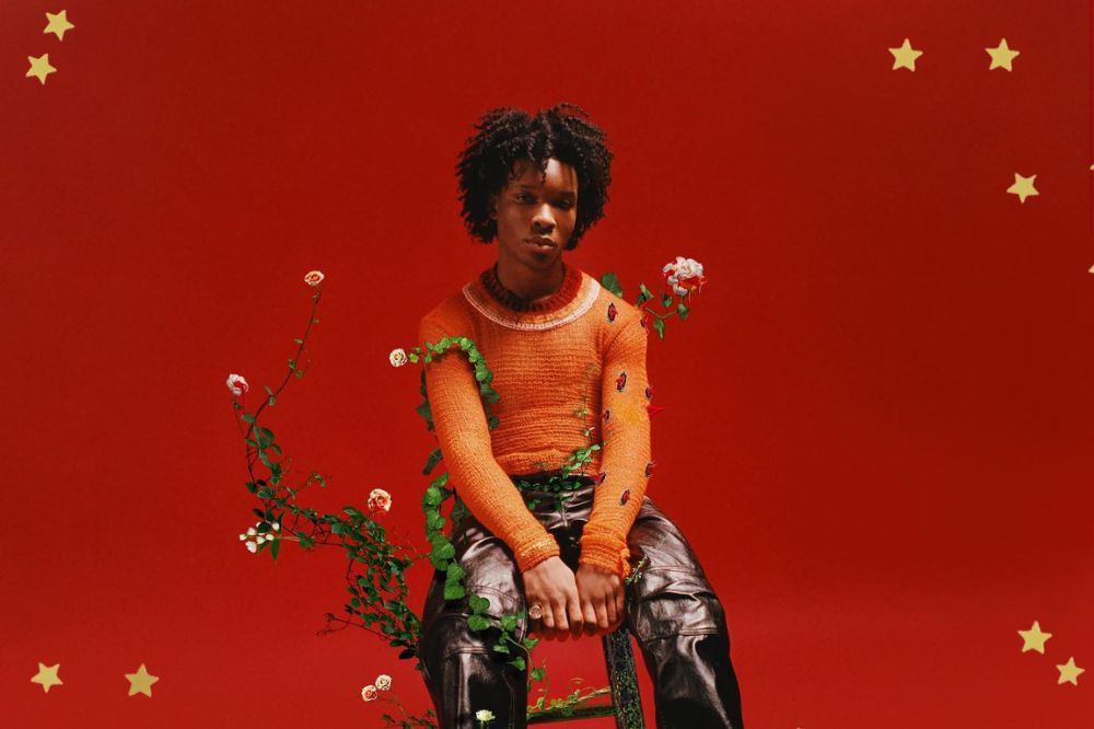 Cantor d4vid em capa de disco posando para foto em um fundo vermelho enquanto está sentado com expressão séria; estrelas amarelas decoram a imagem