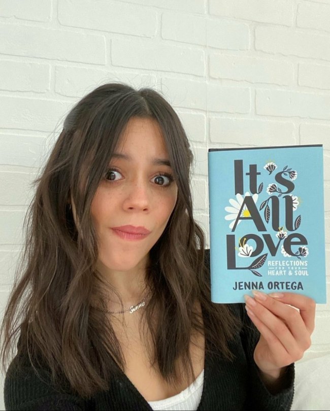 Jenna Ortega segurando o seu livro 'It's All Love' com capa azul