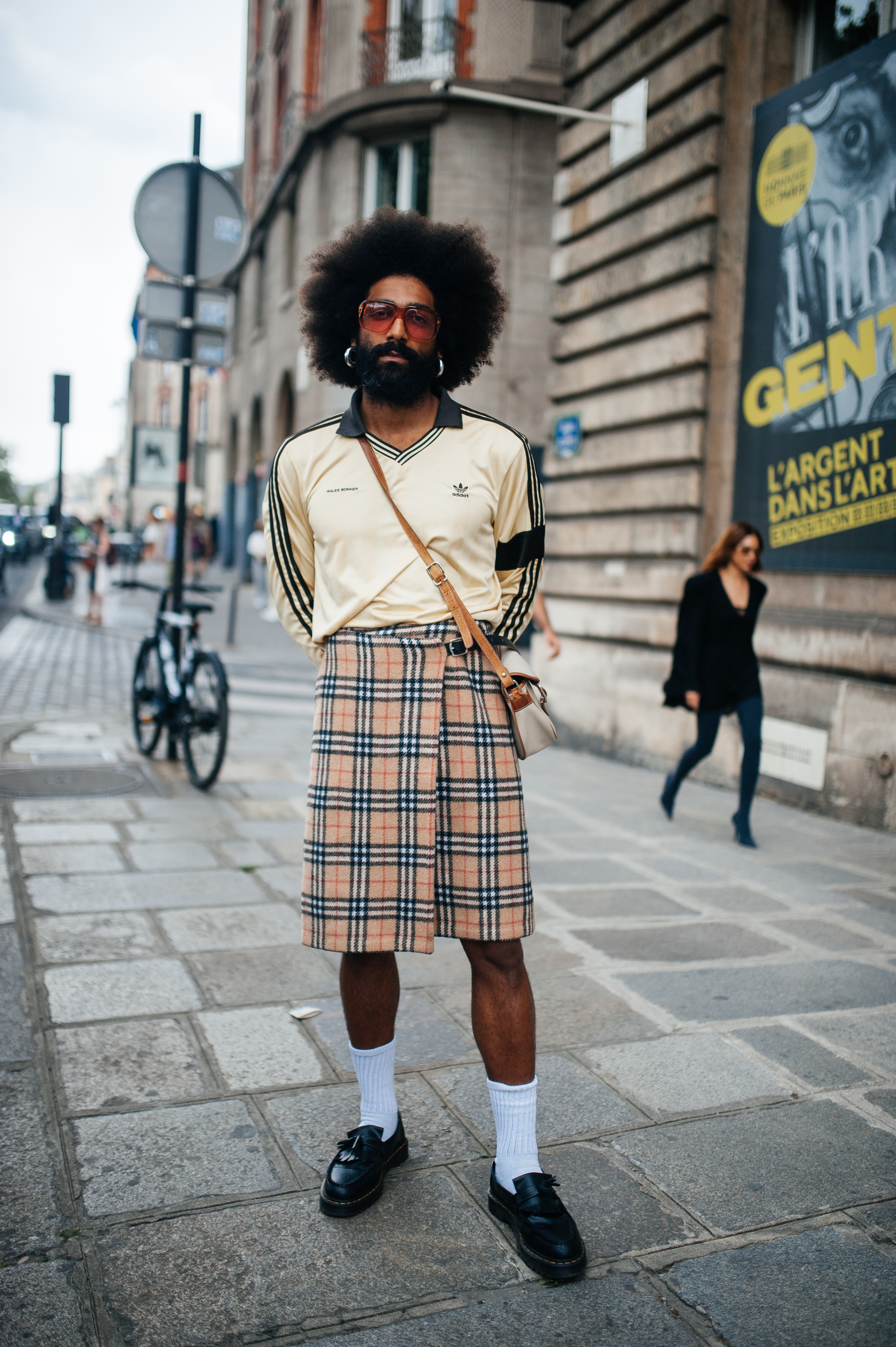 Look no street style da semana de moda masculina de Paris. Homem usando camisa Adidas, saia xadrez e meia branca com tênis