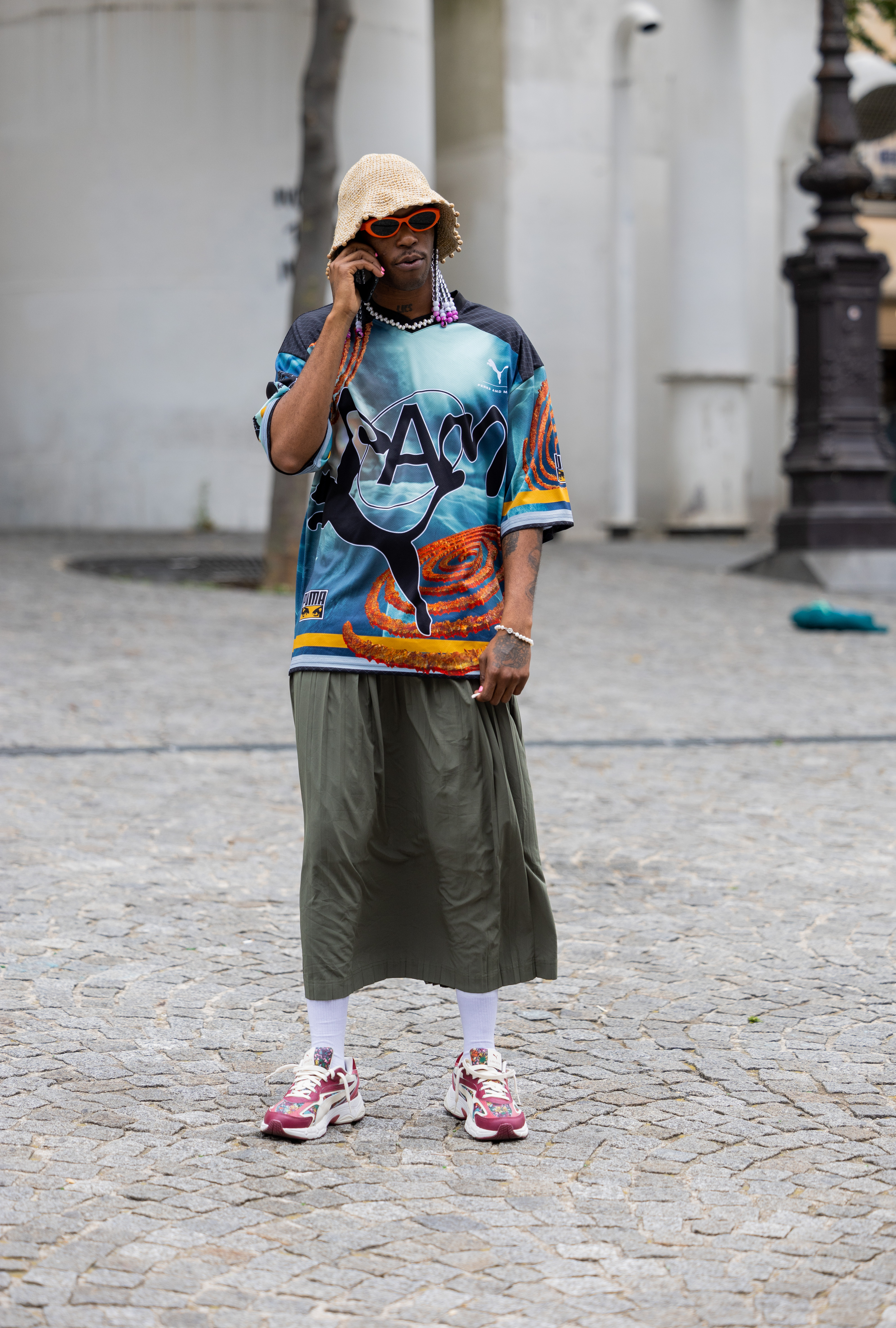 Look no street style da semana de moda masculina de primavera-verão 2024 em Paris. Homem usando camiseta estampada, saia midi e meia branca com tênis esportivo