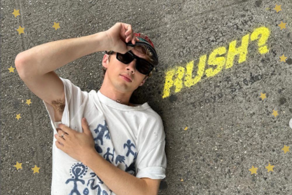 Foto de Troye Sivan no chão ao lado do escrito em amarelo "Rush?". Estrelas douradas adicionadas ao redor.