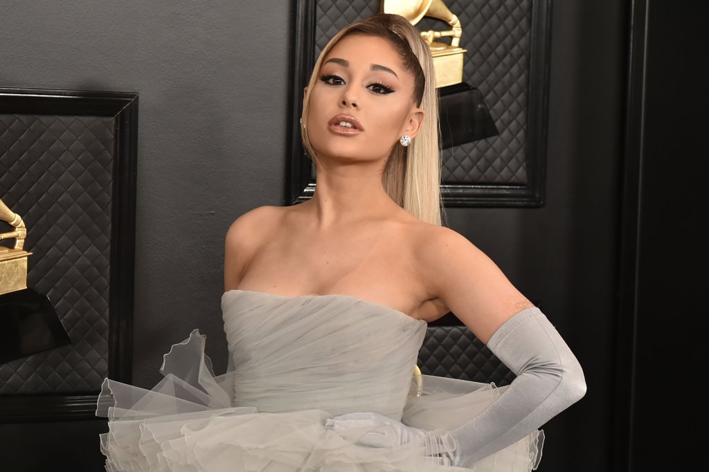 Ariana Grande posando para foto com vestido cinza e luvas da mesma cor; ela está passando pelo tapete vermelho do Grammy