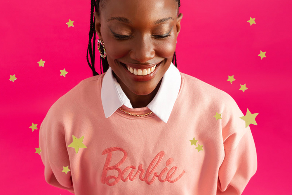 Coleção da C&A inspirada em Barbie; garota usando moletom rosa com camisa branca por baixo e fundo de estrelinhas douradas