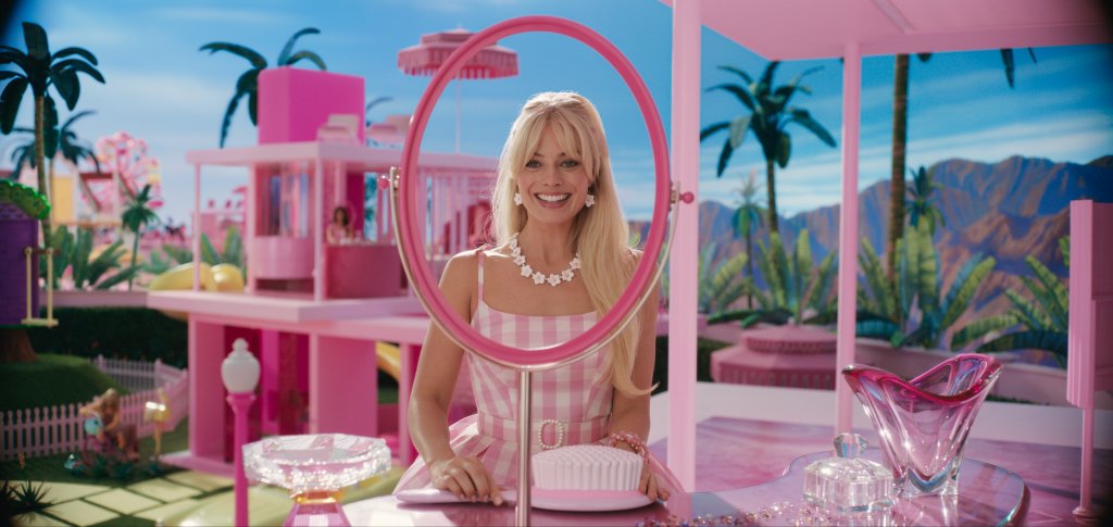 Barbie se olhando em uma moldura de espelho em uma penteadeira em sua "Casa dos Sonhos"; ela está sorrindo e usando um vestido xadrez rosa e branco