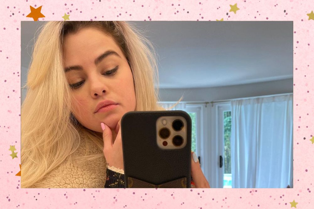 Selena Gomez tirando foto no espelho com o cabelo loiro e expressão neutra; a margem é uma textura rosa com bolinhas; estrelas amarelas e laranjas decoram a imagem