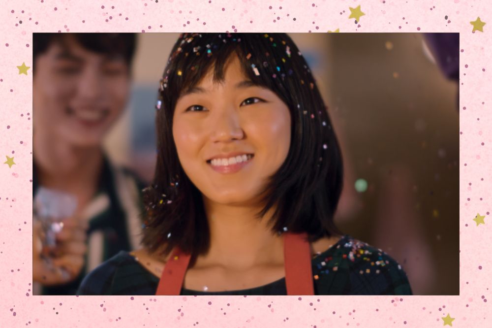 Sharon Cho sorrindo em cena de Além do Guarda-Roupa com confetes caindo ao seu redor; a margem é uma textura rosa com bolinhas; estrelas amarelas decoram a imagem