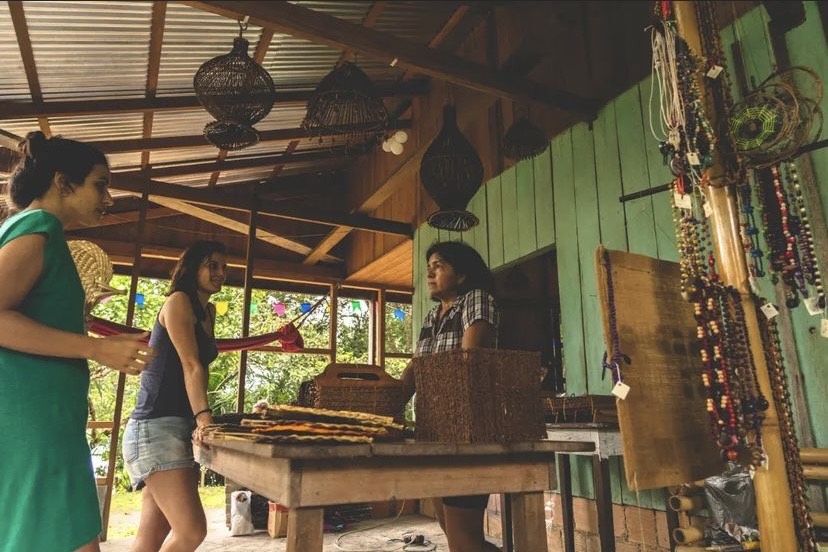 Duas mulheres conversam com uma vendedora de artesanato