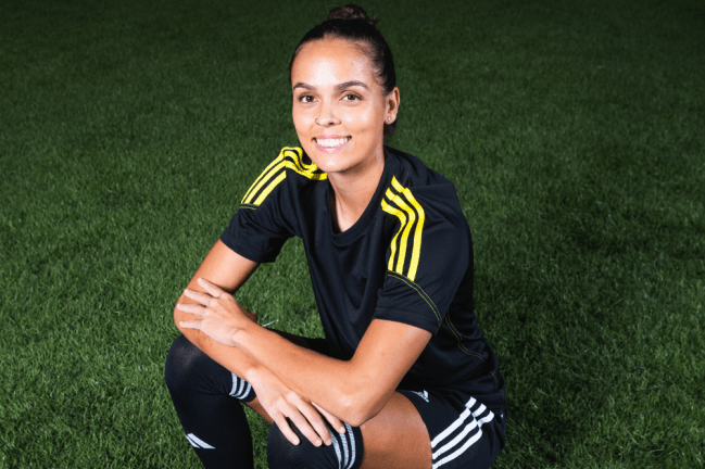 Jogadora de futebol sorri, sentada em gramado