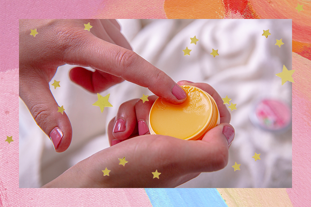 Mão passando cera nutritiva para cutículas. Montagem em fundo rosa, azul e laranja com estrelinhas douradas