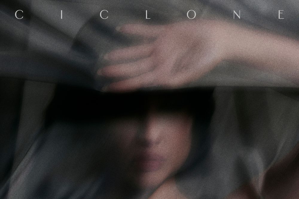 Juliette posando para foto enrolada em tecidos na cor cinza; o nome do álbum CICLONE está escrito em branco na parte superior central da imagem