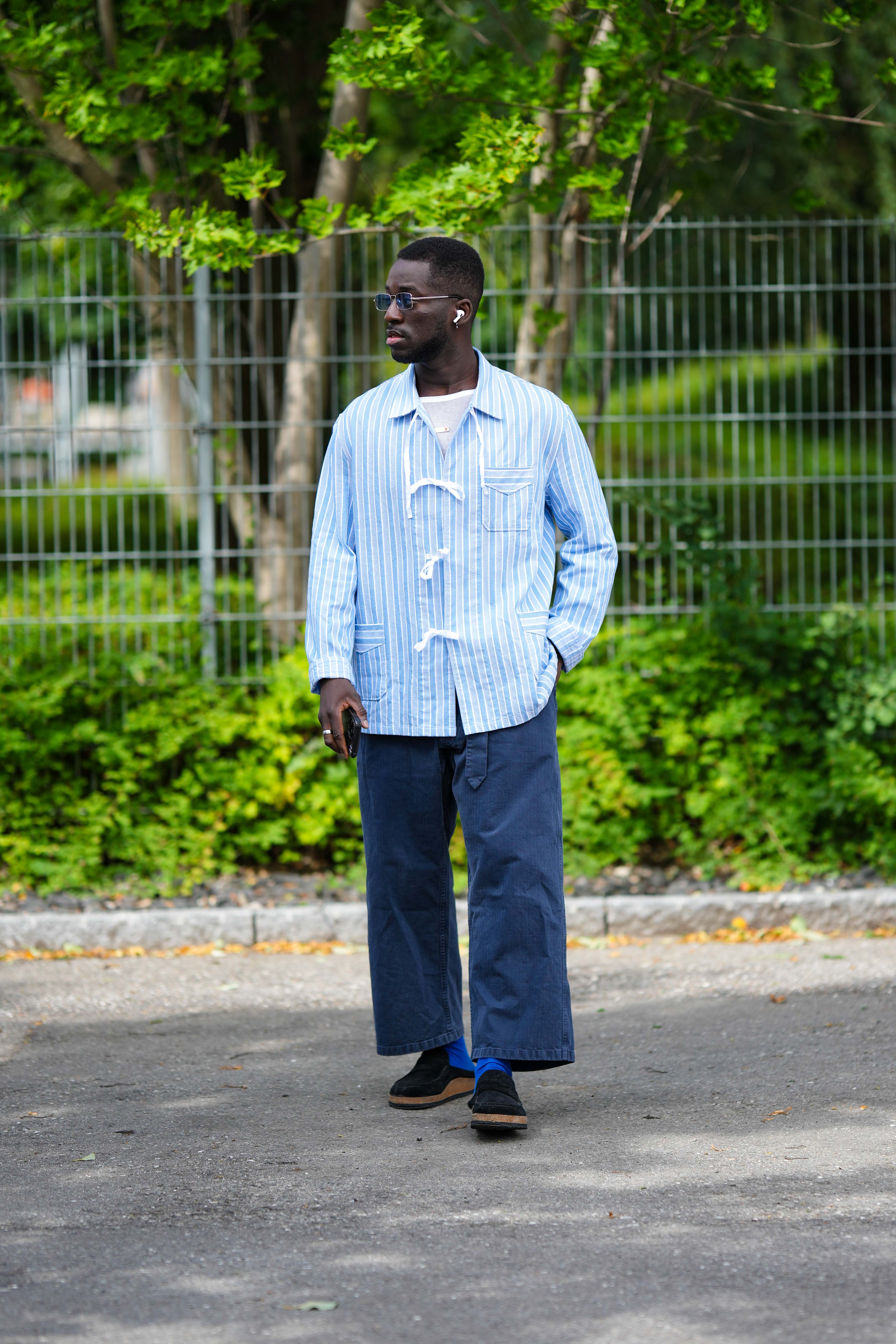 Look da semana de moda de Copenhagen na temporada de primavera-verão 2024. Homem está usando camisa azul com laços e calça jeans