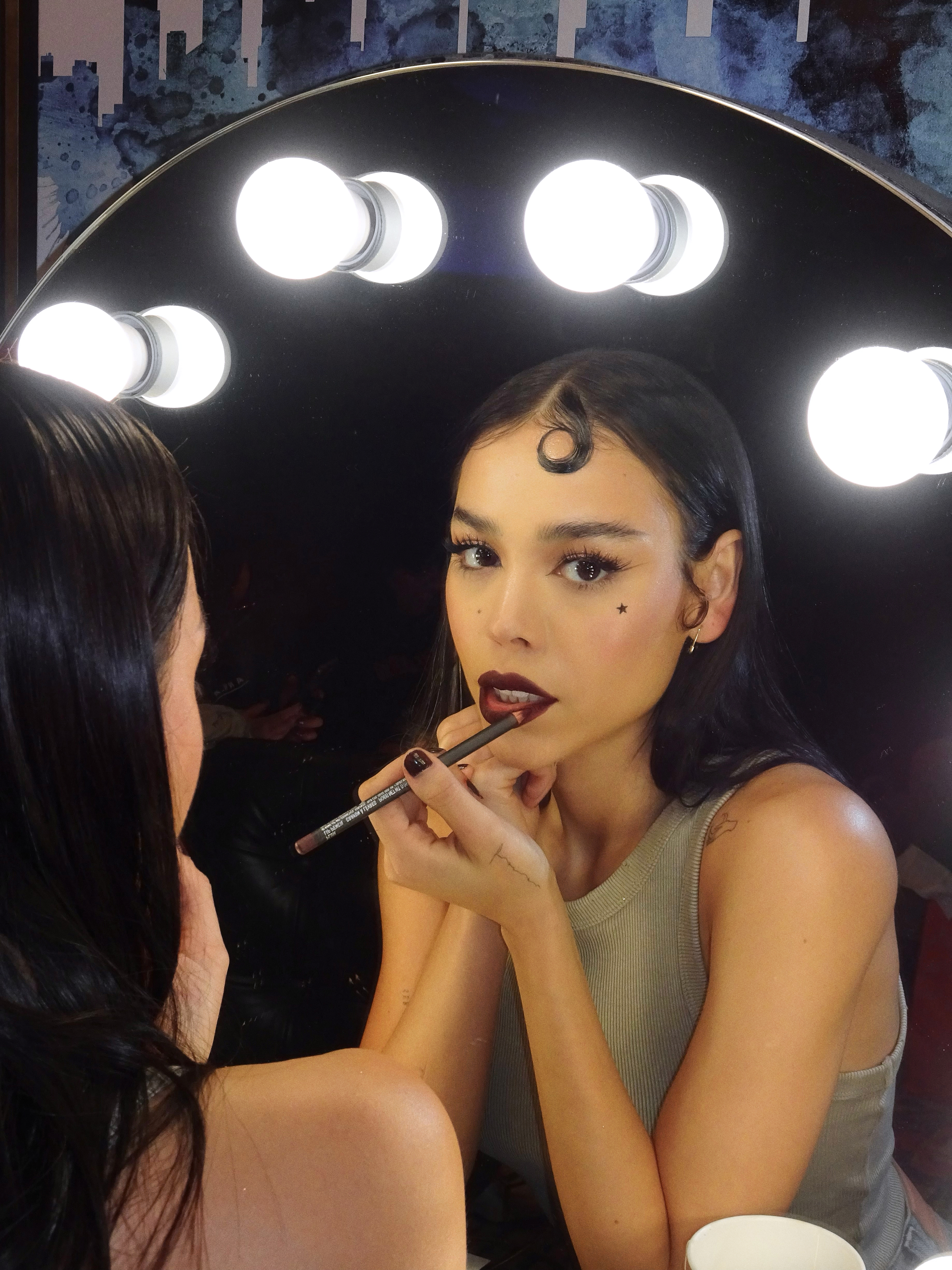 Danna Paola passando batom em frente a um espelho com luzes