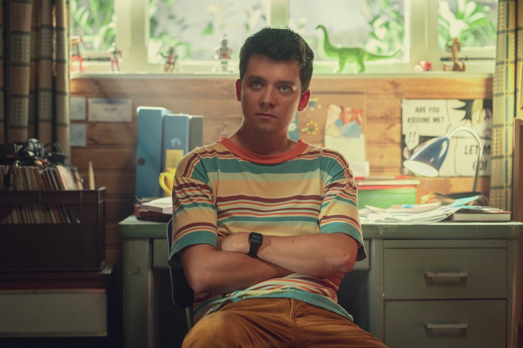 Otis sentado com os braços cruzados e com expressão séria em cena da 4ª temporada de Sex Education