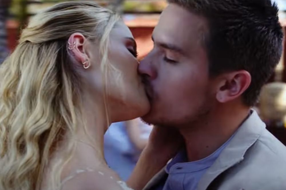 Virginia Gardner e Dylan Sprouse em cena de Belo Casamento; eles estão de olhos fechados enquanto se beijam