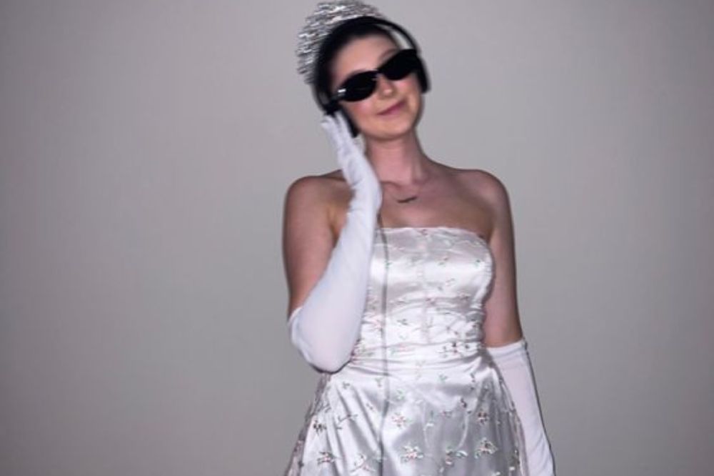 Menina vestida de 'Diário da Princesa' com vestido e luvas brancas, fone de ouvido, óculos de sol e tiara.