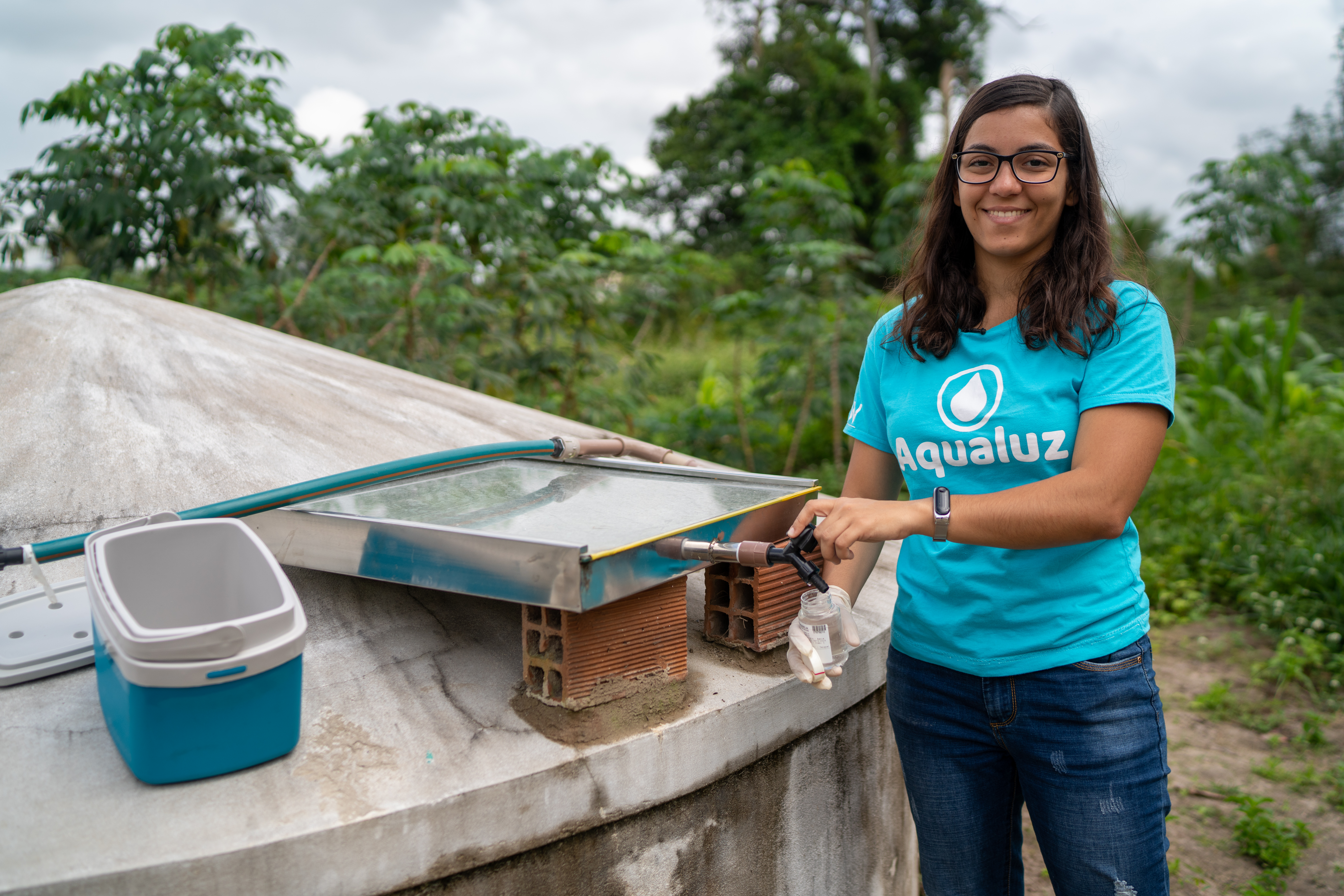 aqualuz Uma jovem enchendo um copo d'água em um sistema de limpeza da água com a luz solar