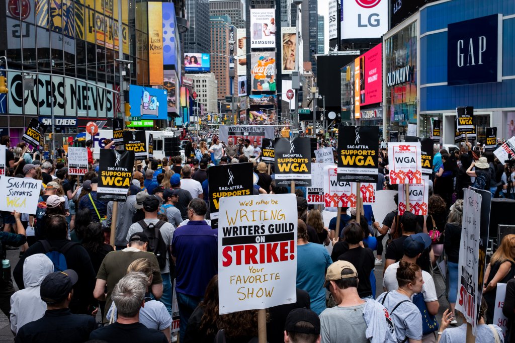 Grupo de pessoas reunidas da Times Square, em Nova Iorque, com cartazes da greve dos roteiristas e atores