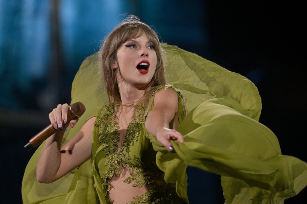 Taylor Swift na The Eras Tour; ela está usando um vestido verde enquanto dança e canta no palco