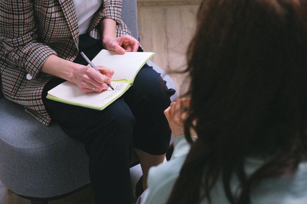 Psicóloga fazendo anotações em um caderno à frente de uma paciente
