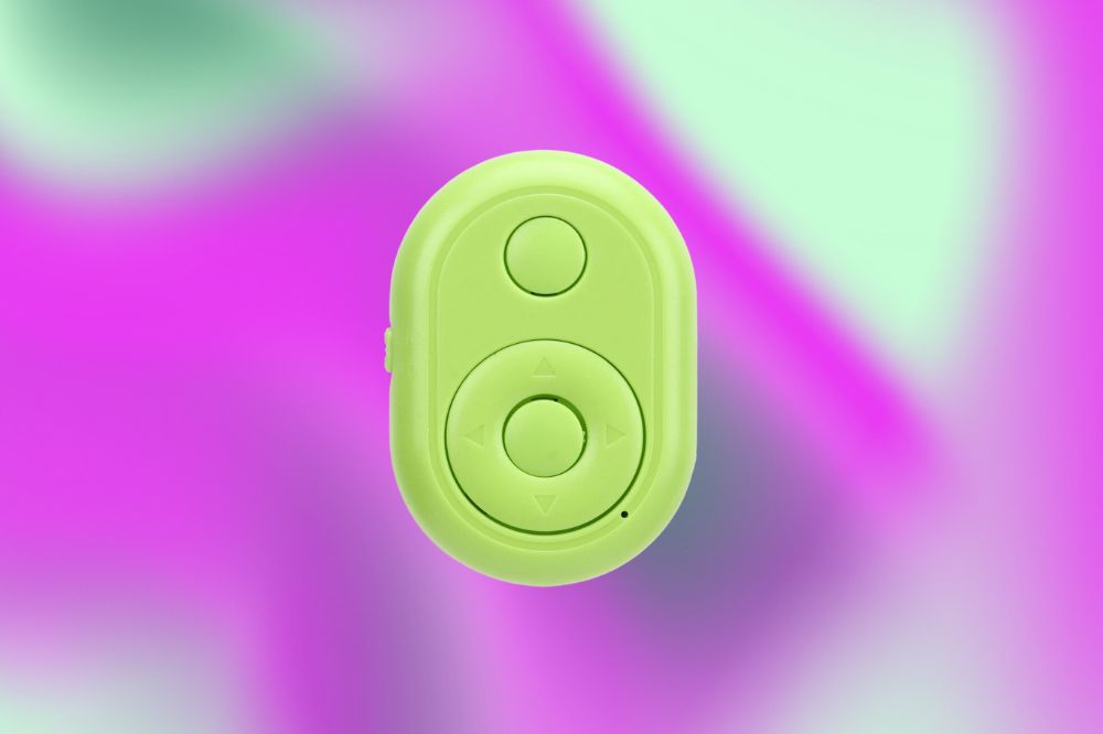 Um controle redondo e verde pequeno, com dois botões: em cima um menor e em baixo, um maior, com setas para cima, para baixo e dos dois lados