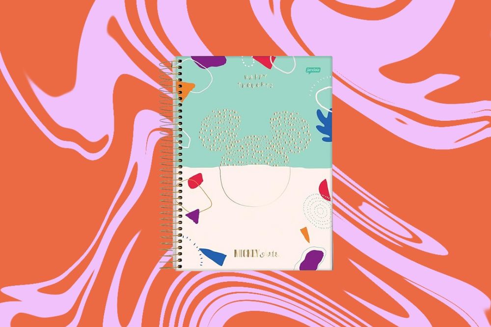 Caderno metade azul claro e metade branco, com o rosto do Mickey desenhado ao meio e elementos coloridos ao redor, em um fundo laranja e rosa