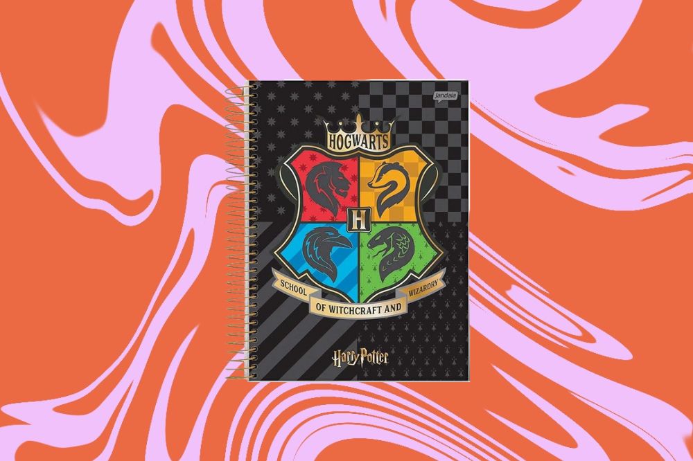 Caderno com a temática de Harry Potter, com as quatro casas de Hogwarts desenhadas ao meio com fundo preto, em um fundo laranja e rosa