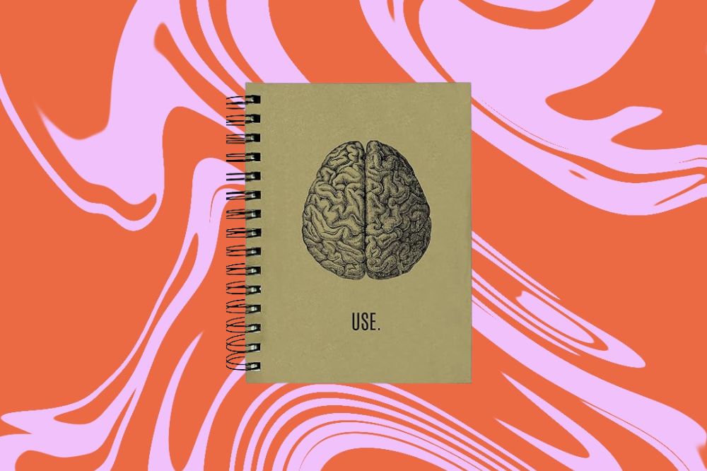 Caderno marrom com a imagem de um cérebro desenhado ao meio em um fundo laranja e rosa