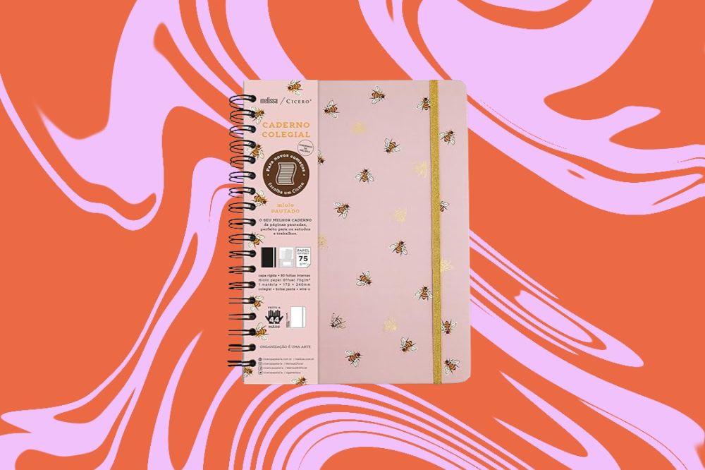 Caderno rosa com estampa de mini abelhas desenhadas em torno dele, em um fundo laranja e rosa