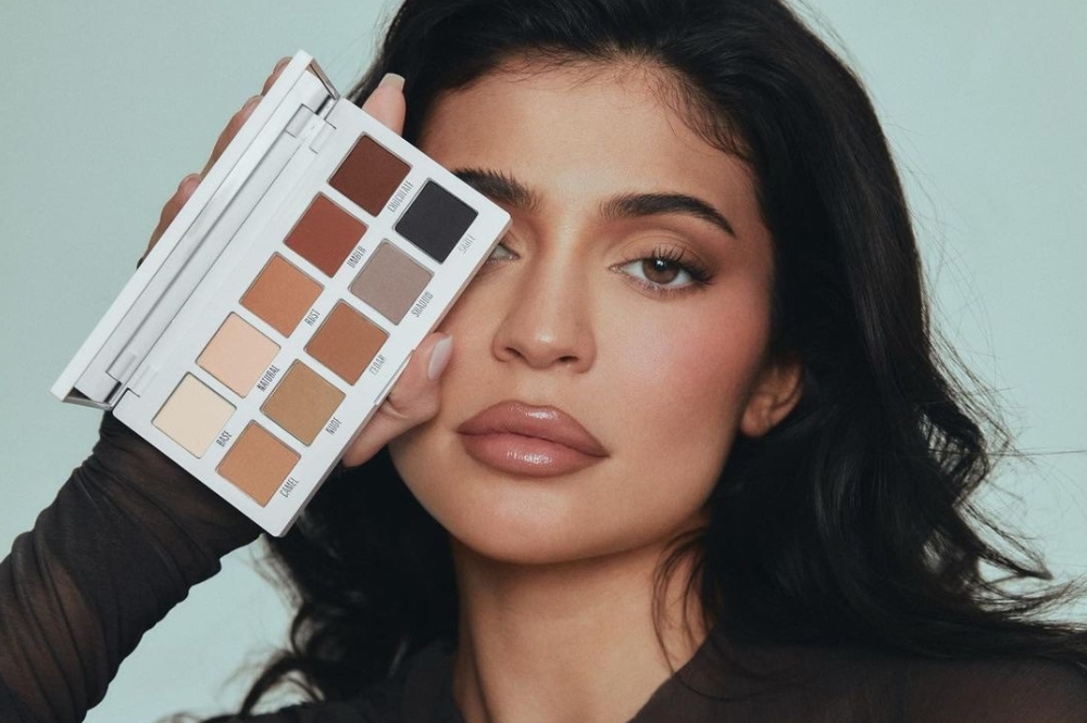 Kylie Jenner segurando paleta de sombras de cores neutras com uma das mãos em frente a um dos olhos