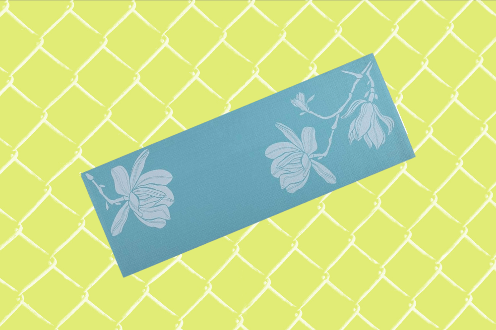 Em um fundo verde claro, há um tapete de yoga azul com detalhes florais.