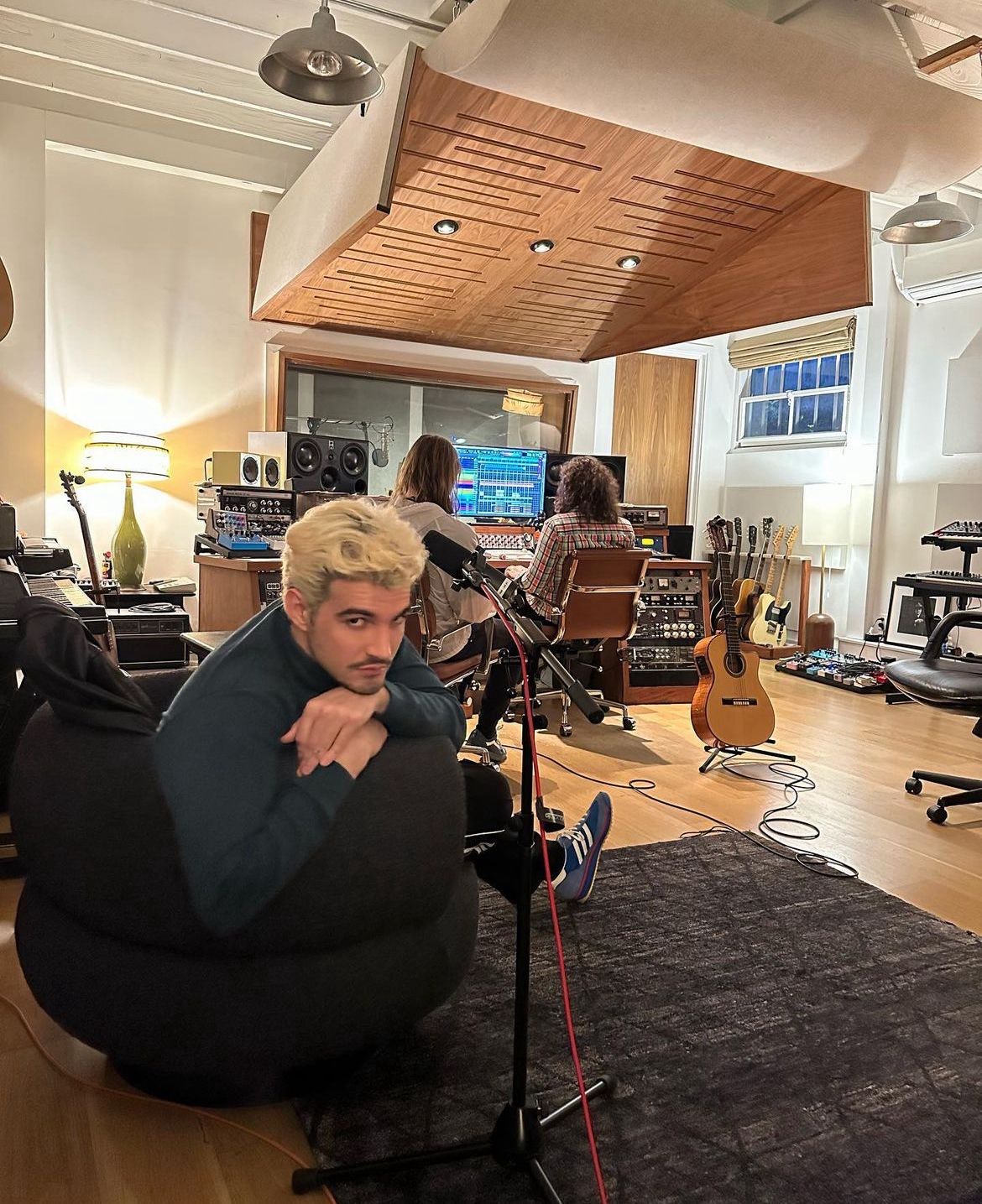 Jão posando para foto em estúdio de gravação com duas pessoas sentadas ao fundo