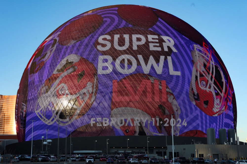Arena Sphere, em Las Vegas, exibindo o logo e a data do Super Bowl LVIII; elementos como capacetes de futebol americano estão na imagem
