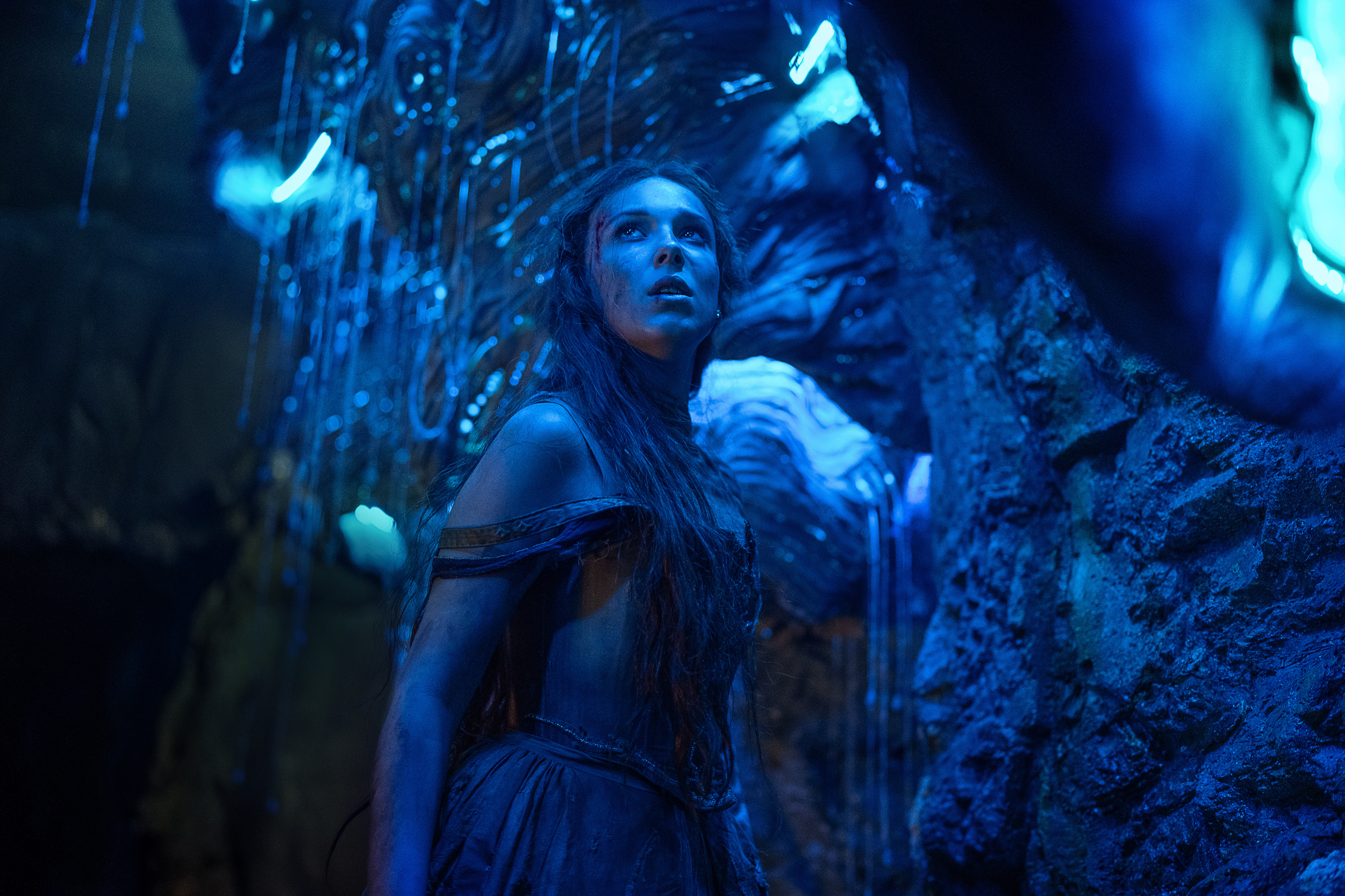 Millie Bobby Brown em cena de Donzela; ela está em uma caverna iluminada por luzes na cor azul