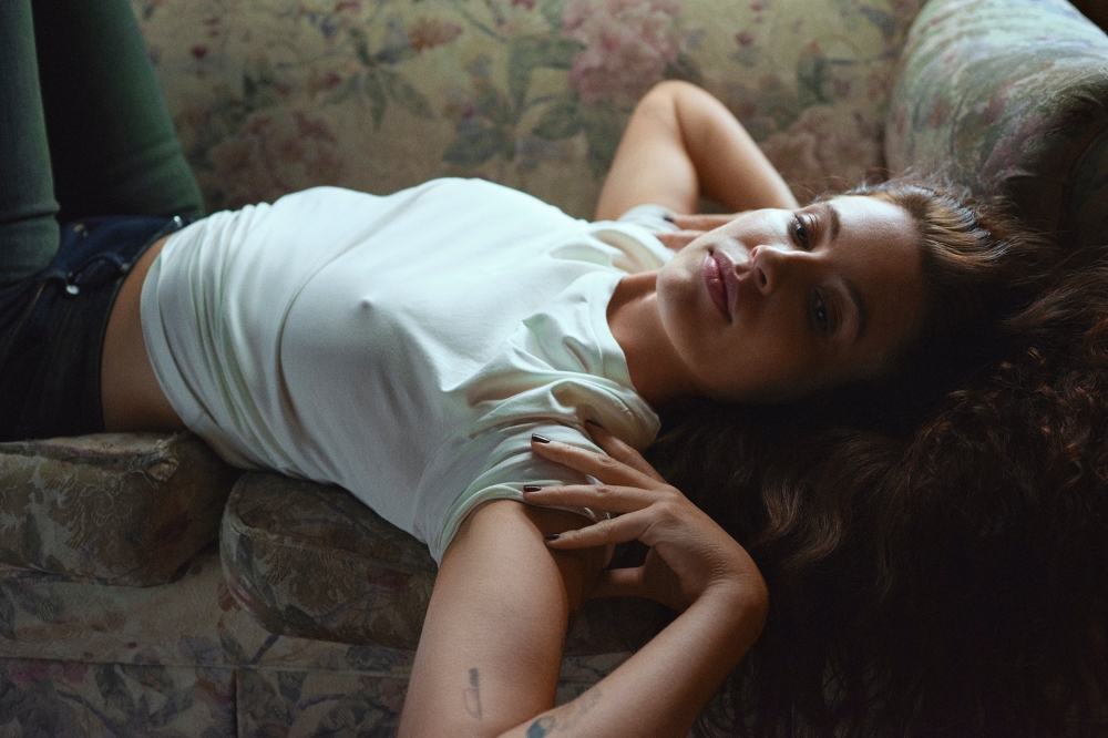 Cantora Fletcher deitada em sofá usando camiseta branca e calça jeans