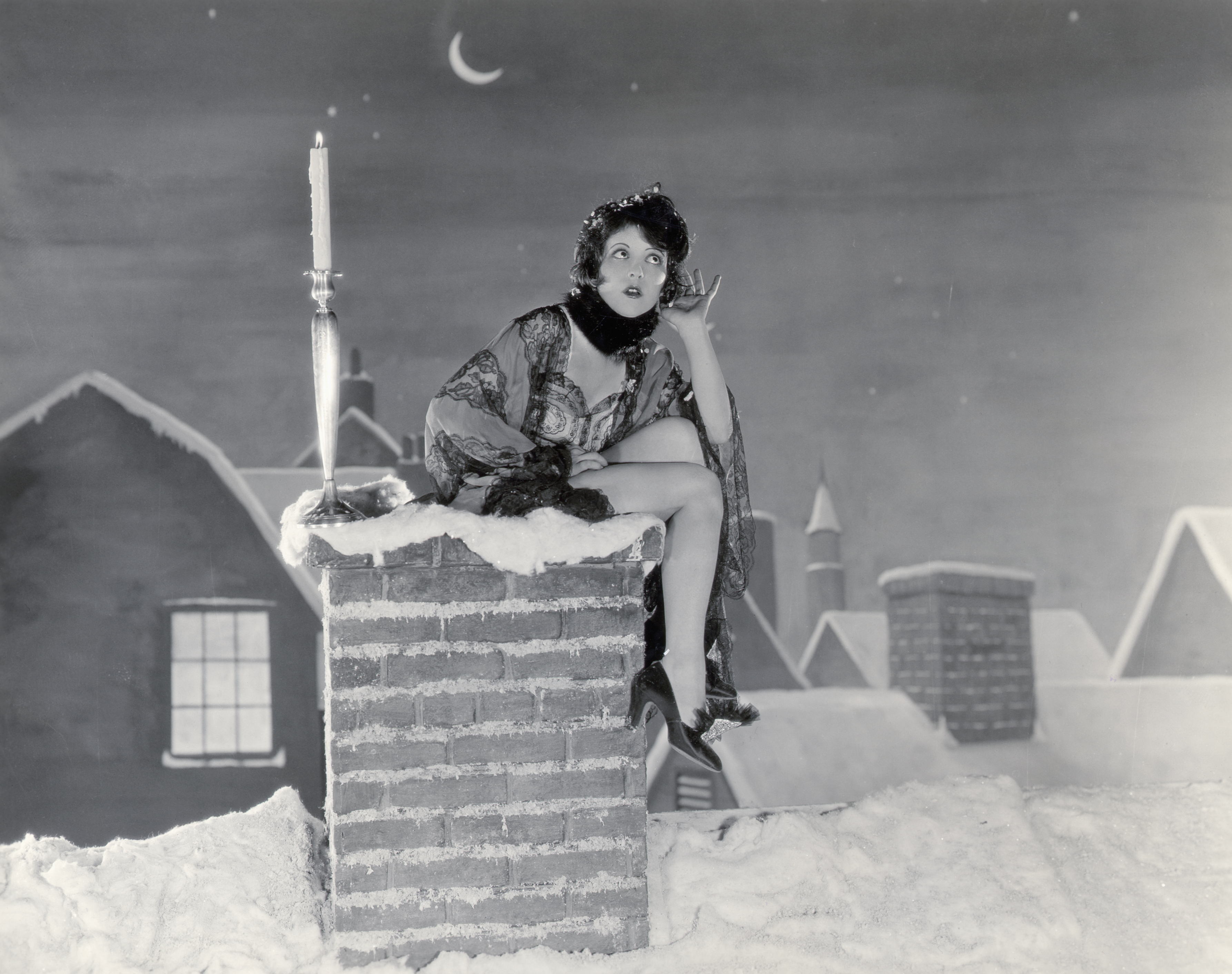 Clara Bow em frame de filme; ela está sentada em uma chaminé com neve durante a noite