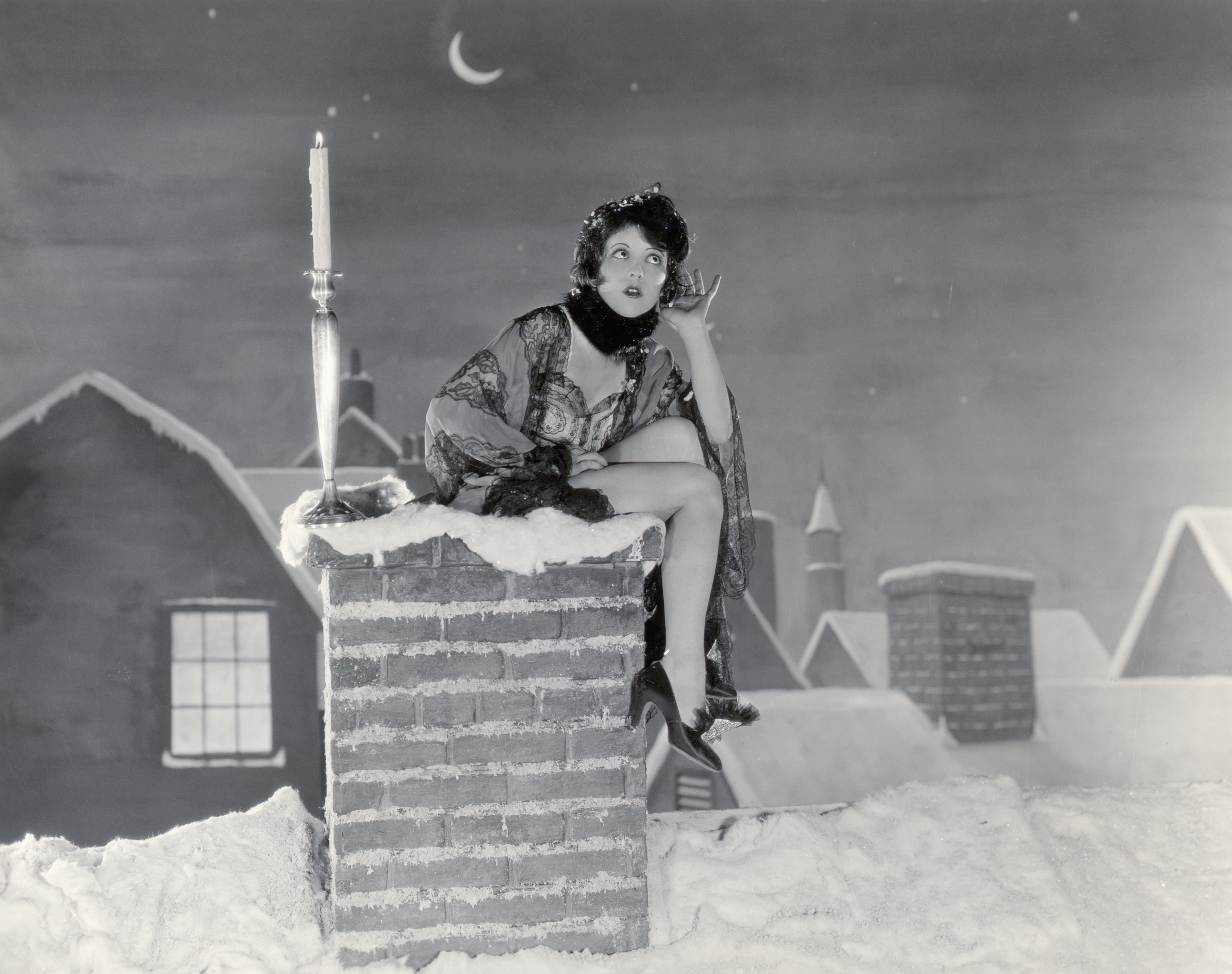 Clara Bow Sitting On Chimney For Santa Clara Bow em frame de filme; ela está sentada em uma chaminé com neve durante a noite