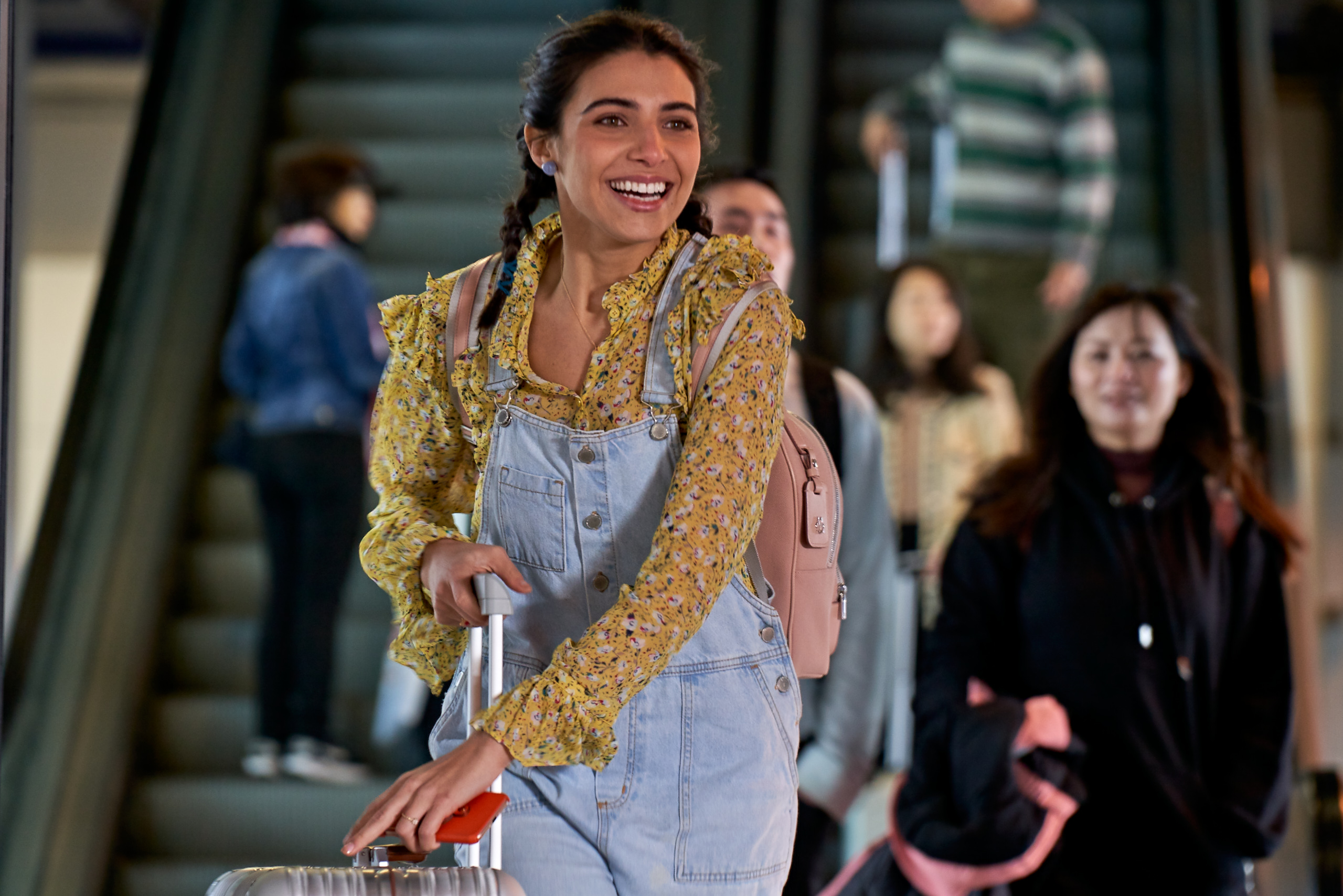 Rayssa Bratillieri em cena de The Modelizer; ela está sorrindo enquanto corre no aeroporto com mala